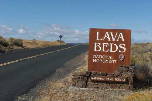 Sign for Lava Beds National Monument along a road, with a clear blue sky and sparse vegetation in the background.