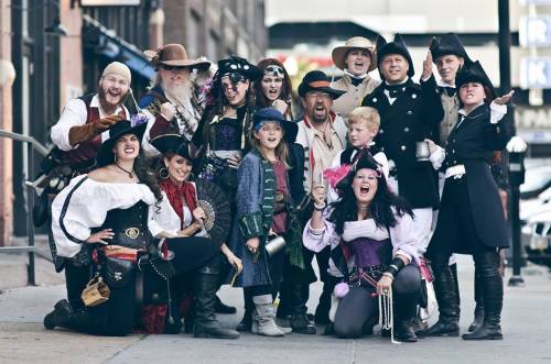 A lively group of people in pirate and historical costumes posing together outdoors, smiling and having fun.