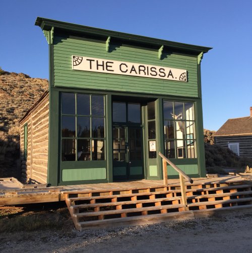 A green wooden building with the sign "The Carissa" on a sunny day, surrounded by hills.