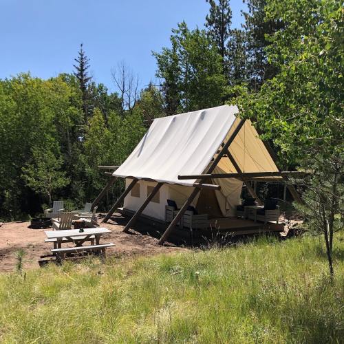 A canvas tent on a wooden platform surrounded by trees, with a picnic table nearby in a grassy area.