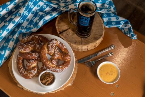 A plate of soft pretzels with mustard and cheese dip, alongside a mug of dark beer on a wooden table.