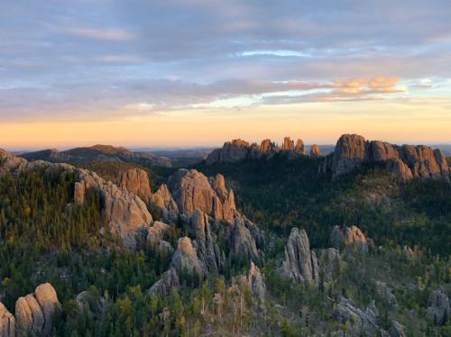 A scenic view of rugged mountains and forested hills under a colorful sunset sky.