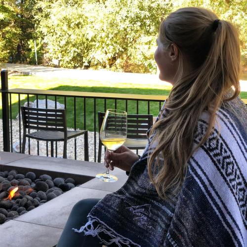 A person sits by a fire pit, wrapped in a blanket, enjoying a drink in a serene outdoor setting.