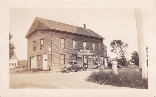 Historic black-and-white photo of a two-story wooden building with a vintage car parked outside.