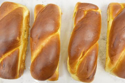 Four freshly baked, golden-brown braided loaves of bread arranged in a row on a baking sheet.
