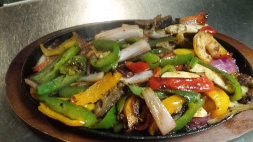 Sizzling platter of colorful sautéed bell peppers, onions, and grilled vegetables.