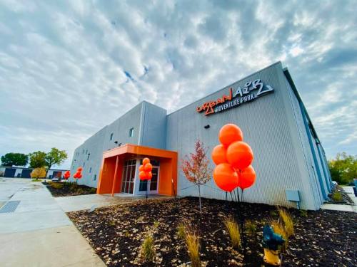 Exterior of an adventure park building with orange balloons and a cloudy sky.