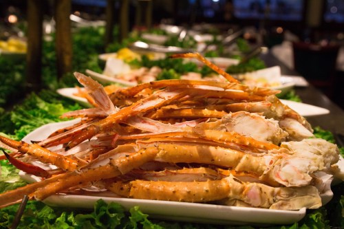 A platter of cooked crab legs arranged on a bed of lettuce, with various dishes in the background.