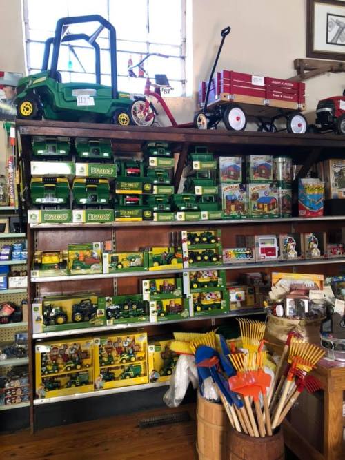 A wooden shelf filled with toy tractors, wagons, and colorful children's tools in a vintage store.
