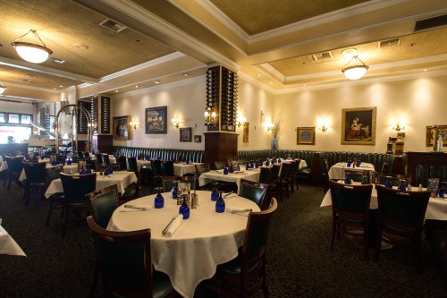 Elegant restaurant interior with round tables, blue glassware, and decorative artwork on the walls. Warm lighting ambiance.