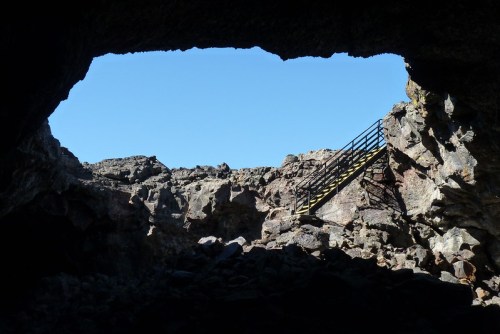 View from inside a cave, showing rocky terrain and a staircase leading up to the bright blue sky.