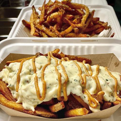 A serving of fries topped with creamy sauce and drizzled with a tangy dressing, alongside a container of plain fries.