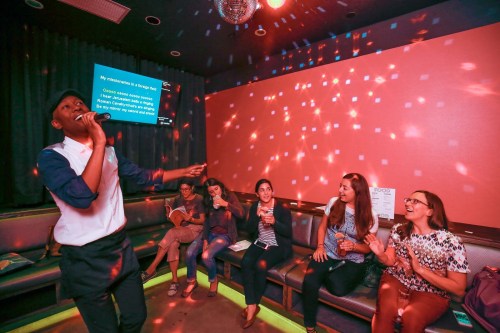 A group of friends enjoys karaoke in a vibrant room with colorful lights, singing and having fun together.