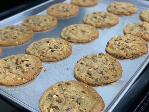 Freshly baked cookies with chocolate chips and nuts on a silver baking sheet.