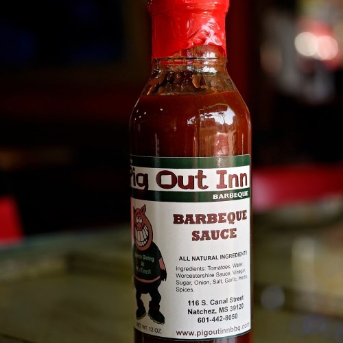 A bottle of Pig Out Inn barbecue sauce with a cartoon pig logo and ingredient list on the label.