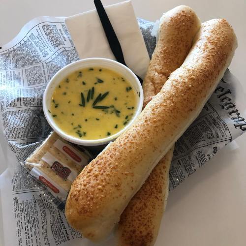 A bowl of creamy soup with chives, two breadsticks, and a packet of crackers on a paper tray.