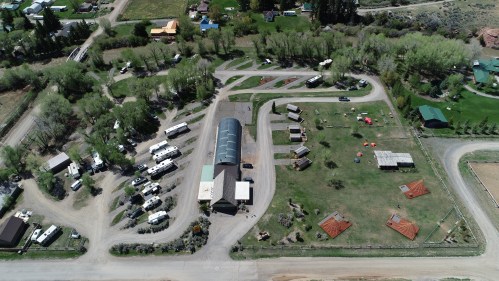 Aerial view of a rural campground with RVs, cabins, and green spaces surrounded by trees and roads.