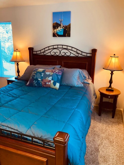 Cozy bedroom featuring a wooden bed with a blue quilt, two lamps, and a wall art above the bed.