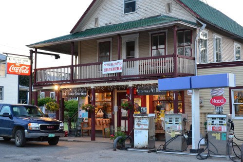 A quaint gas station and store with a porch, featuring a sign for "creemees" and vintage gas pumps outside.