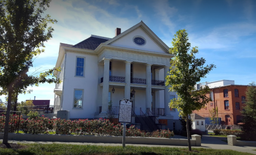 Historic white mansion with columns, surrounded by greenery and flowers, under a clear blue sky.