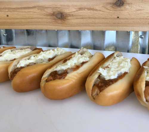 A row of hot dog buns filled with a creamy topping and a savory filling, placed on a white surface.