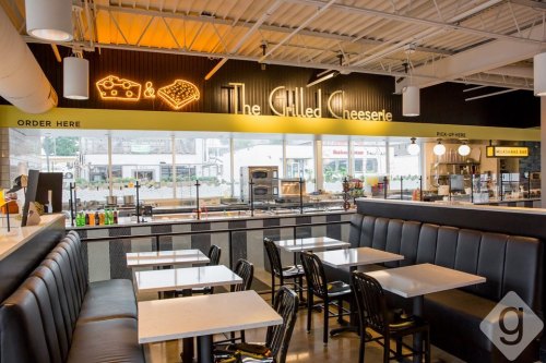 Interior of a modern eatery with black booths, white tables, and a bright sign reading "The Chilled Cheeserie."
