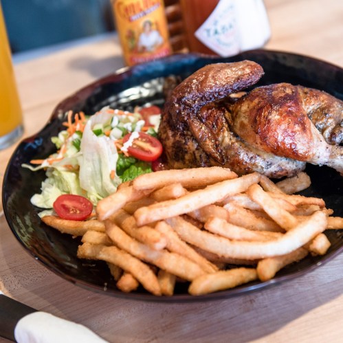 A plate featuring roasted chicken, crispy fries, and a fresh salad with tomatoes, served with sauces in the background.