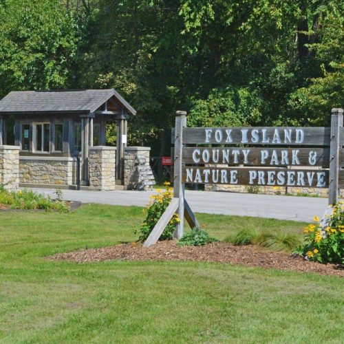 Sign for Fox Island County Park & Nature Preserve, with a visitor center and landscaped greenery in the foreground.