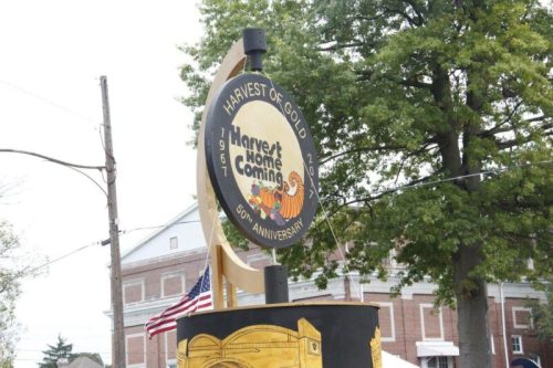 Sign for "Harvest Homecoming" festival, celebrating its 50th anniversary, with colorful decorations and trees in the background.