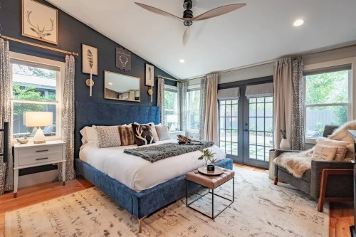 Cozy bedroom featuring a blue bed, large windows, a rug, and stylish decor, creating a warm and inviting atmosphere.