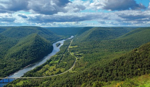 A scenic view of a winding river surrounded by lush green hills and a blue sky with fluffy clouds.