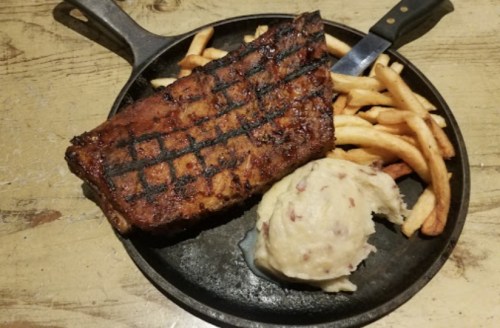 A sizzling steak on a cast iron plate, served with fries and creamy mashed potatoes.