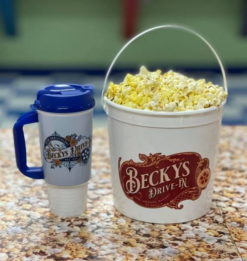 A large bucket of popcorn next to a blue travel mug, both featuring the "Becky's Drive-In" logo.