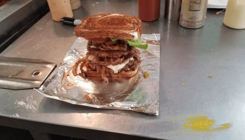 A towering sandwich with multiple beef patties, lettuce, tomato, and sauce, served on toasted bread.