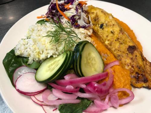 A plate featuring grilled fish, rice, salad, cucumbers, pickled onions, and a vibrant orange puree.