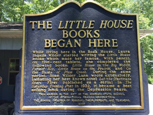 Sign commemorating the origin of the Little House books by Laura Ingalls Wilder, detailing her writing journey.
