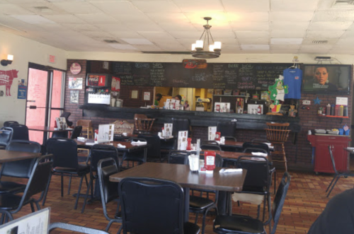 Interior of a casual restaurant with empty tables, a counter, and a chalkboard menu on the wall.