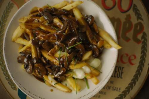 A plate of French fries topped with mushroom gravy and garnished with chives, set on a decorative background.
