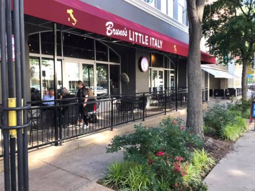 Exterior view of Bruno's Little Italy restaurant, featuring outdoor seating and a red awning, surrounded by greenery.