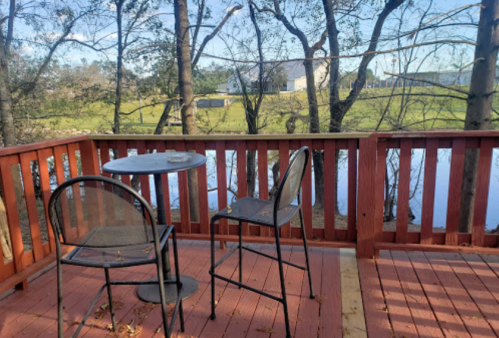 A wooden deck with two chairs and a small table overlooking a serene pond surrounded by trees.
