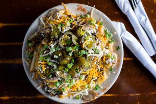 A plate of nachos topped with cheese, jalapeños, green onions, and various toppings on a wooden table.