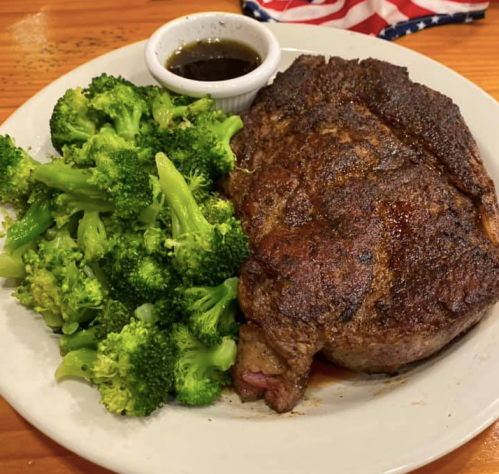 A plate featuring a seasoned steak alongside steamed broccoli and a small bowl of sauce.