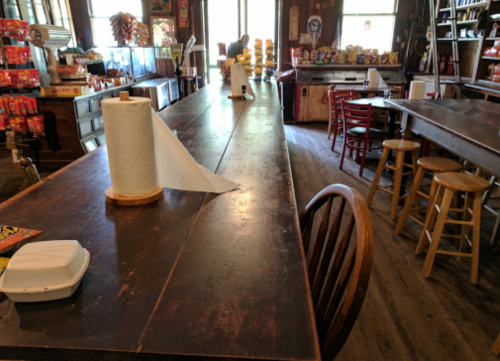 A rustic diner interior with wooden tables, chairs, and a long counter, featuring paper towels and a cozy atmosphere.