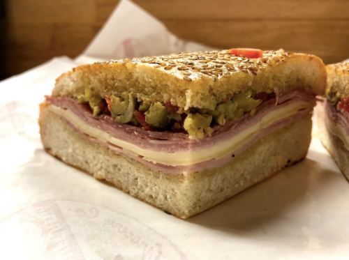 A cross-section of a sandwich with layers of meats, cheese, and toppings, served on a sesame seed bun.