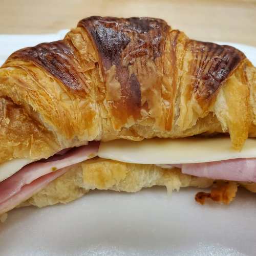 A close-up of a croissant sandwich filled with ham and cheese, resting on a white plate.