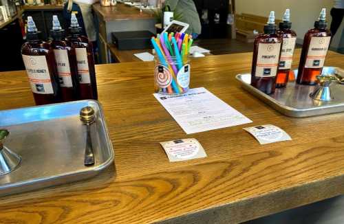 A wooden counter with bottles, colorful pens, a paper, and small cards arranged neatly.