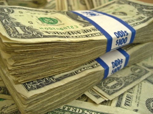 Stacks of one-dollar bills bundled with blue bands, surrounded by more cash.