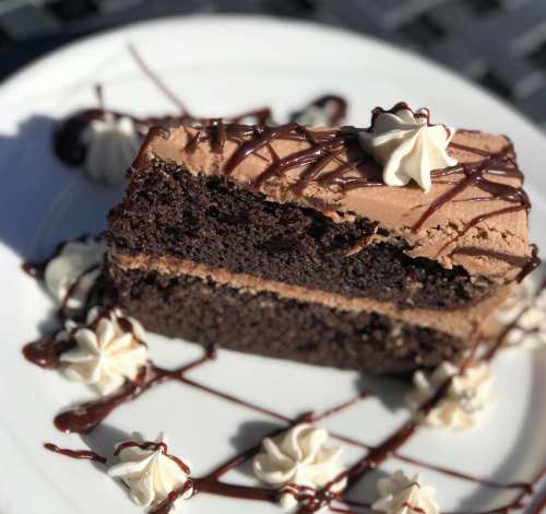 A slice of chocolate cake with creamy frosting and drizzled chocolate sauce, garnished with whipped cream.