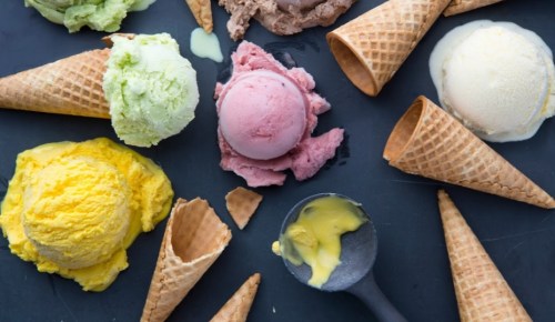 Colorful scoops of ice cream in various flavors, arranged with waffle cones on a dark surface.