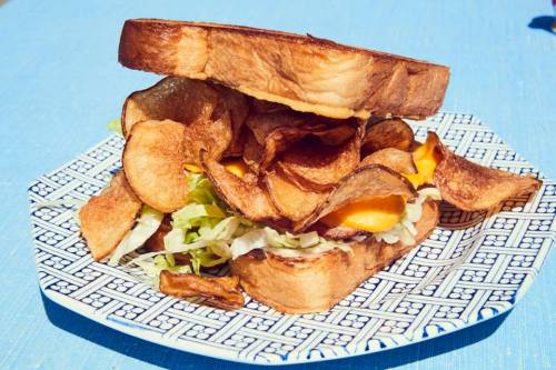 A stacked sandwich with lettuce and cheese, topped with crispy potato chips, served on a decorative plate.